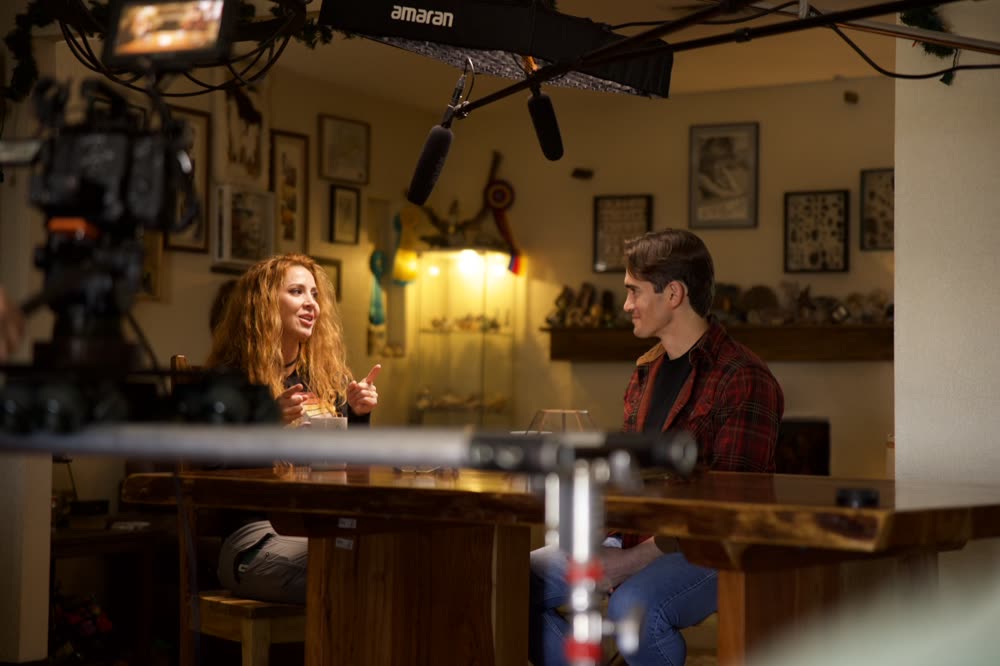 Andrew interviewing a guest on set, camera and boom in frame